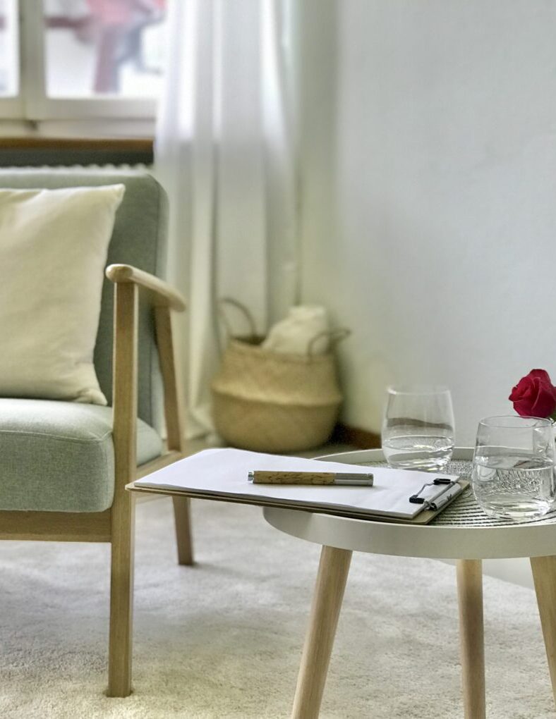 Sessel mit Kissen, daneben steht ein Couchtisch mit Schreibzeug, Wassergläsern und Blumen